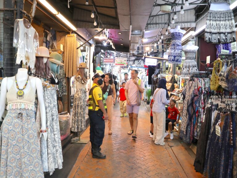 Visitors walking past clothing stalls along a busy Chatuchak market lane