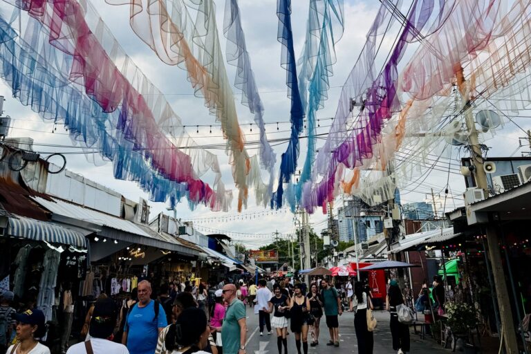 Colorful fabric decorations over a busy aisle at Chatuchak Weekend Market, with people walking below