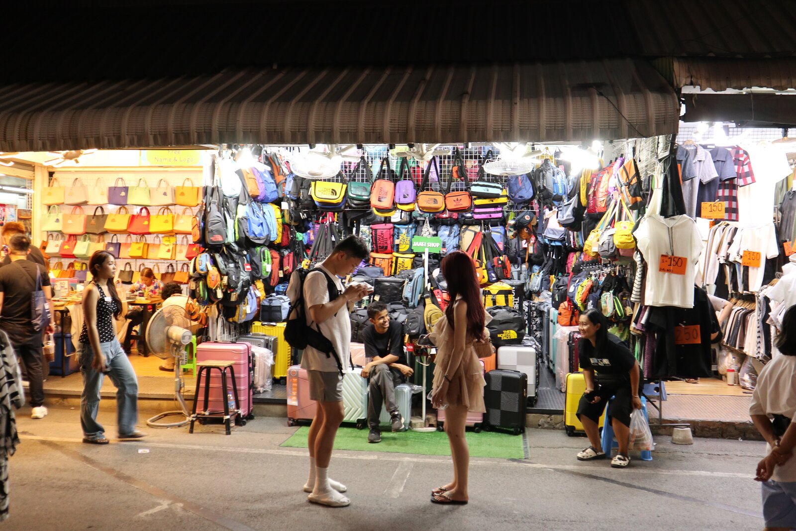 People moving around a brightly lit market stall at night, with two people facing each other in the centre