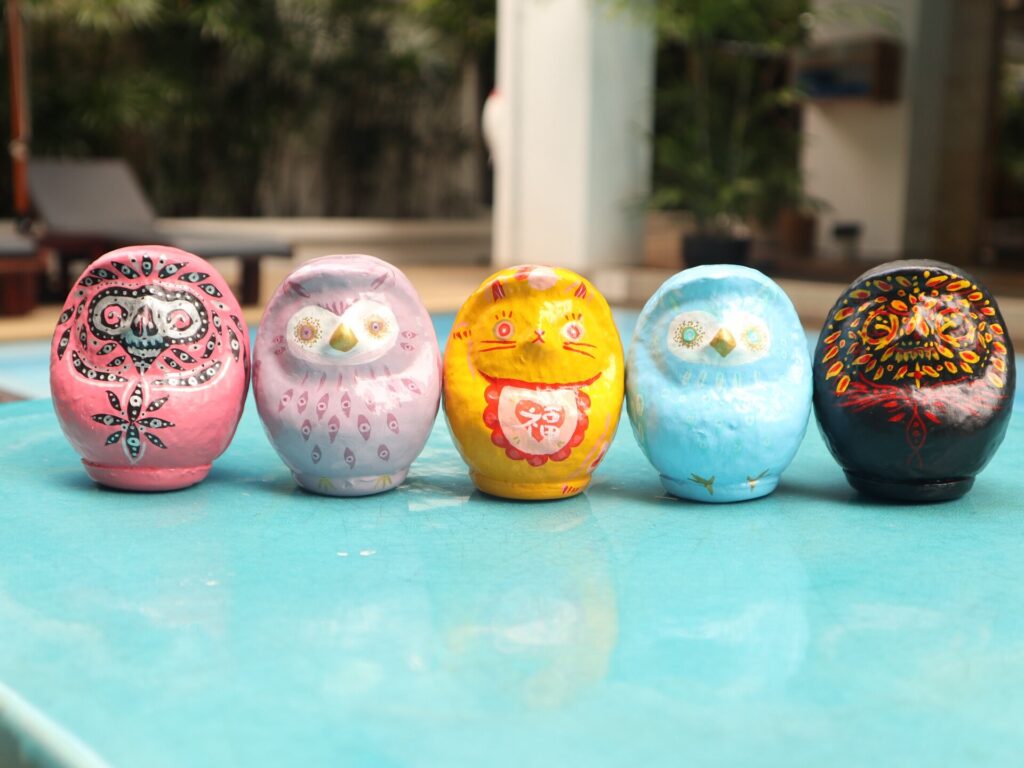 Five Daruma art pieces in pink, purple, yellow, blue and black