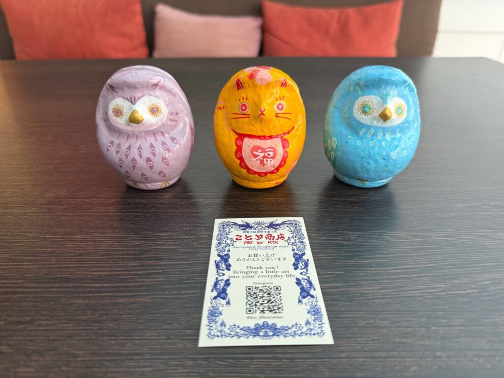 Three Daruma art pieces with a Kotori Shoten artist card