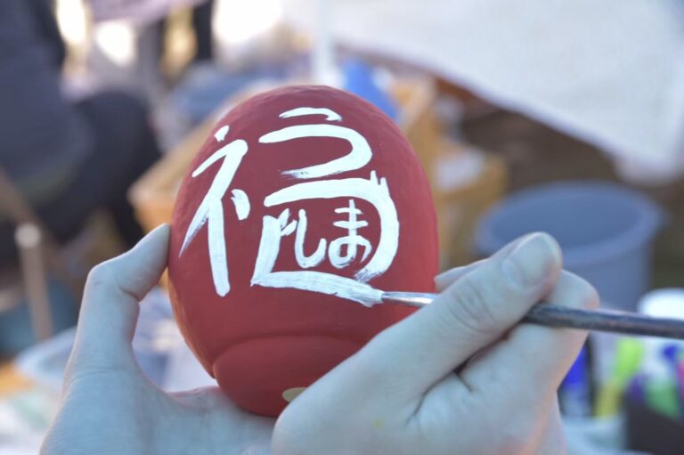 Kotori/KTR hand-painting characters onto a red Daruma