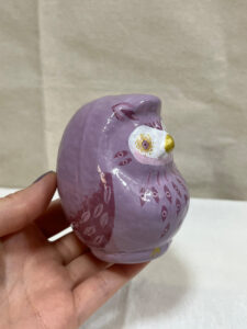 A hand holding a purple owl Daruma art piece, showing repeated eye motifs