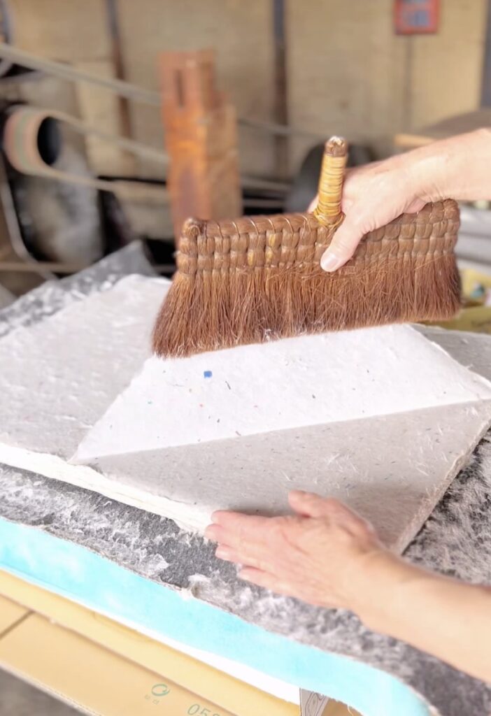 Hands holding a brush over a sheet of washi during paper work.