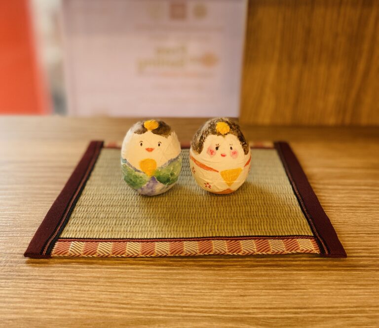 Two small decorated figures displayed on a woven mat.